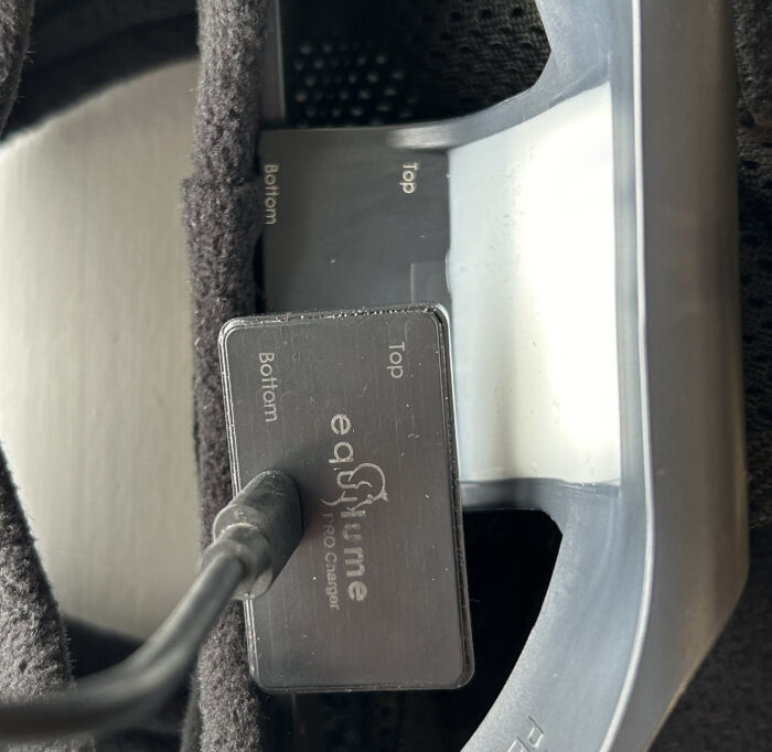 Equilume Pro Wireless charging pad attached to the USB cable is shown above the Equilume Pro Light Mask about to line up to charge.